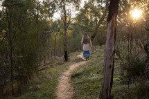 a girl walking on a trail through the woods 