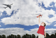 Young caucasian boy playing with a toy plane as a passenger plane flies overhead themes of future imagination inspiration