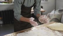 Unrecognizable male baker claps and scatters white flour in the air. Young man making homemade bread claps with a handful of organic whole wheat flour in each hand. Slow motion, close up.