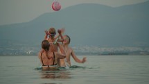 Mother with two children, a boy and a girl, enjoys playing with a ball in the sea against a backdrop of mountains in Greece during evening