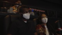 African American couple enjoying film during pandemic, wearing white face masks.