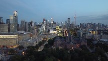 Aerial evening view of dynamic downtown Toronto. Camera right above Queen's Park shows the financial district with moderate traffic. Slight panning shot of drone flying toward the cityscape.