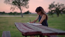 Woman Reading Bible and Journaling Outside at Sunset