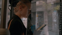 A woman stands near the door on the bus, holds an e-book in her hand and reads it while riding a city bus