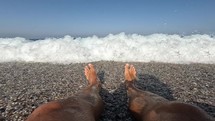 Man lying on rocky beach letting waves hit his legs