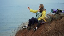 Traveler couple sitting on top of the cliff and posing taking selfie using smartphone.