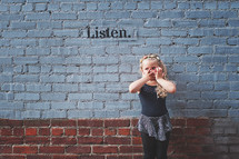a little girl covering her mouth over the word listen 