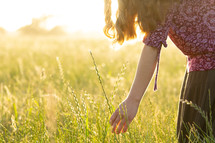 teen girl in a long skirt walking through a field of tall grasses 