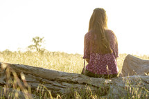 teen girl sitting on a log in a field 