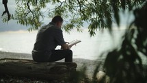 man sitting on a beach reading a Bible and praying 
