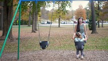 mother pushing her daughter on a swing set 
