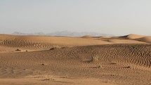 Middle eastern desert, nature landscape with distant mountains. Sand blowing in wind over desert sand dunes in evening desert sunset, sunlight in cinematic slow motion.