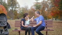 grandfather, granddaughter, and grandmother on a park bench in fall 