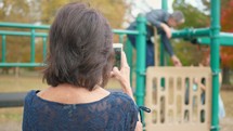 grandmother filming her husband and granddaughter on a playground 