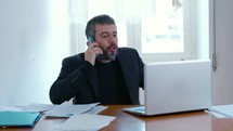 Man sitting at desk with laptop open and talking on the phone.