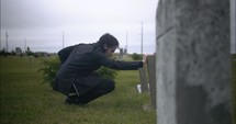 Young, sad man in black suit kneeling in cemetery at graveyard tombstone grieving in cinematic slow motion.