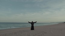 Monk Makes A Spiritual Religious Connection Open Arms At Lonely Beach Near Sea