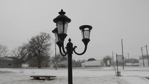 Snowing on old, vintage looking lamp post. Snow falling on cold winter morning in small USA town in cinematic slow motion.