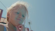 Slow-motion video, close-up from a low angle of a girl blowing a dandelion, making the seeds parachute away.