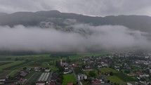 Sweeping left to right drone view over a foggy Dolomite landscape, revealing a church amidst the clouds