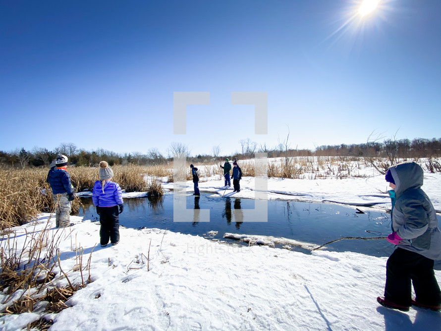 children playing outdoors by a pond in snow 