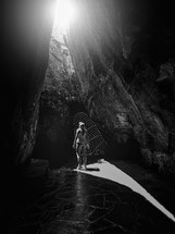 a woman looking up at sunlight in an opening in a cave 