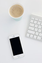 iPhone, latte, and computer keyboard on a white table 