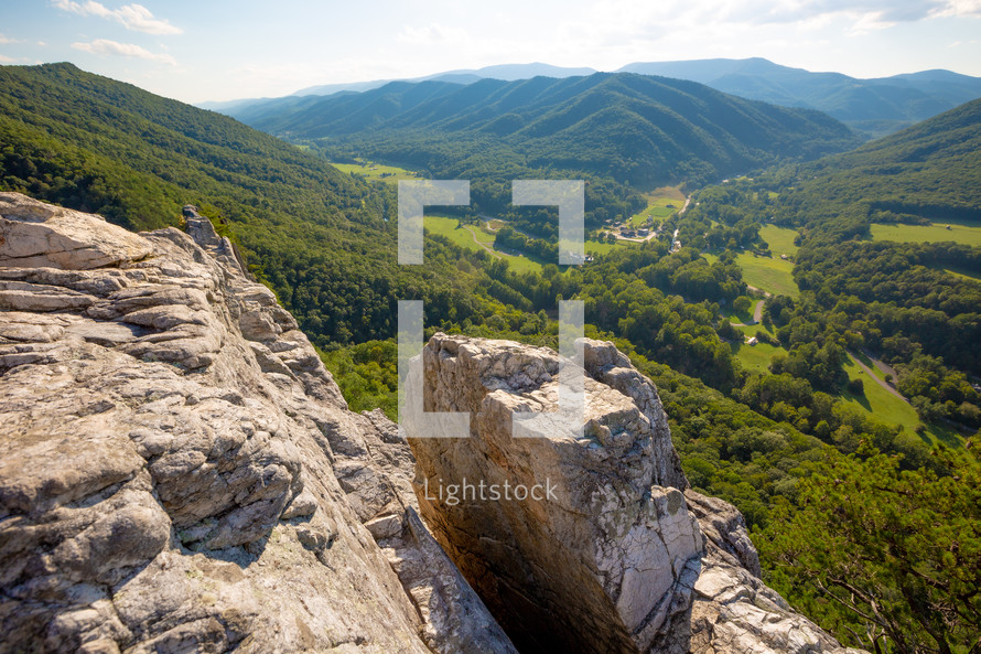 Rocky edge of cliff with outlook view of mountain range and lush green valley with tree in Seneca Rocks