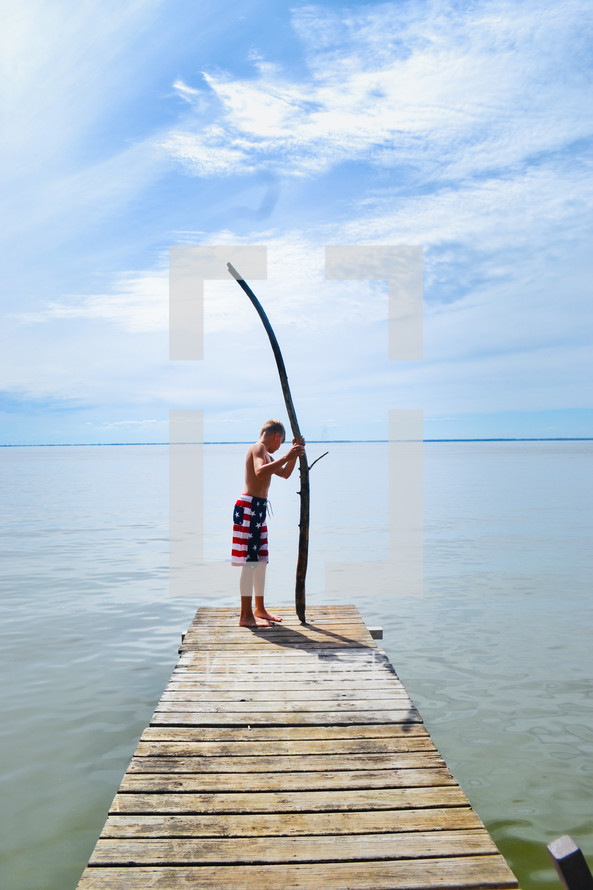 a boy holding a stick standing on a dock 