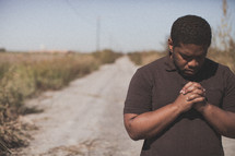 man kneeling in prayer on a dirt road 