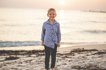 young boy standing on a beach at sunset 