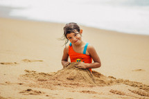 A young girl covering herself with sand on the beach.