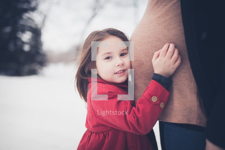 toddler hugging her pregnant mother's belly