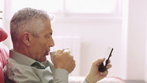 a man drinking coffee and scrolling through a smart phone 