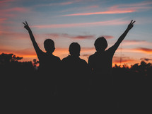 silhouettes of people with hands raised at dusk 