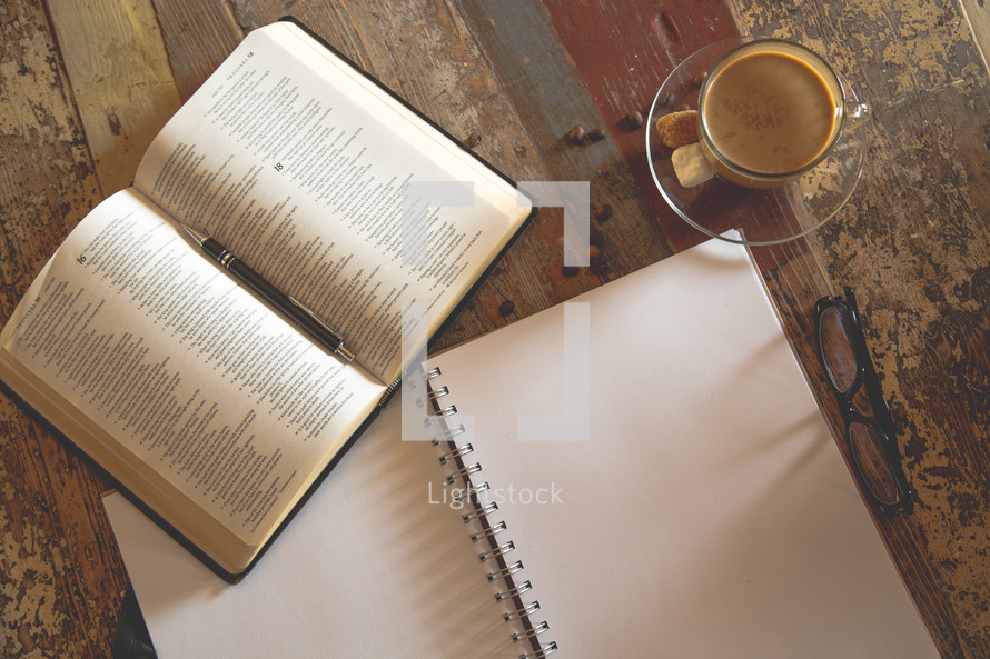 open Bible, blank pages of a journal, and coffee cup on a wood table 