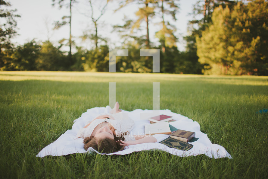 woman lying on a blanket in the grass next to books