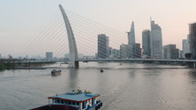 Aerial shot from flying drone of ship floating on the river, cable-stayed bridge and business center with modern skyscrapers in Ho Chi Minh city, early morning time
