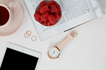 Raspberries in a bowl, watch, tablet, magazine, rings, and coffee cup 
