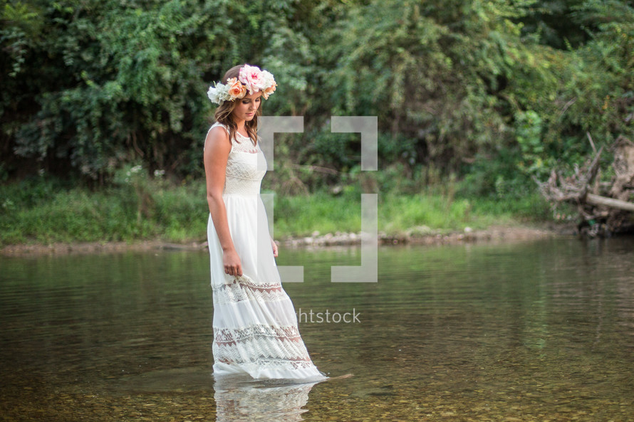 a woman in a white dress with flowers in her walking in water 