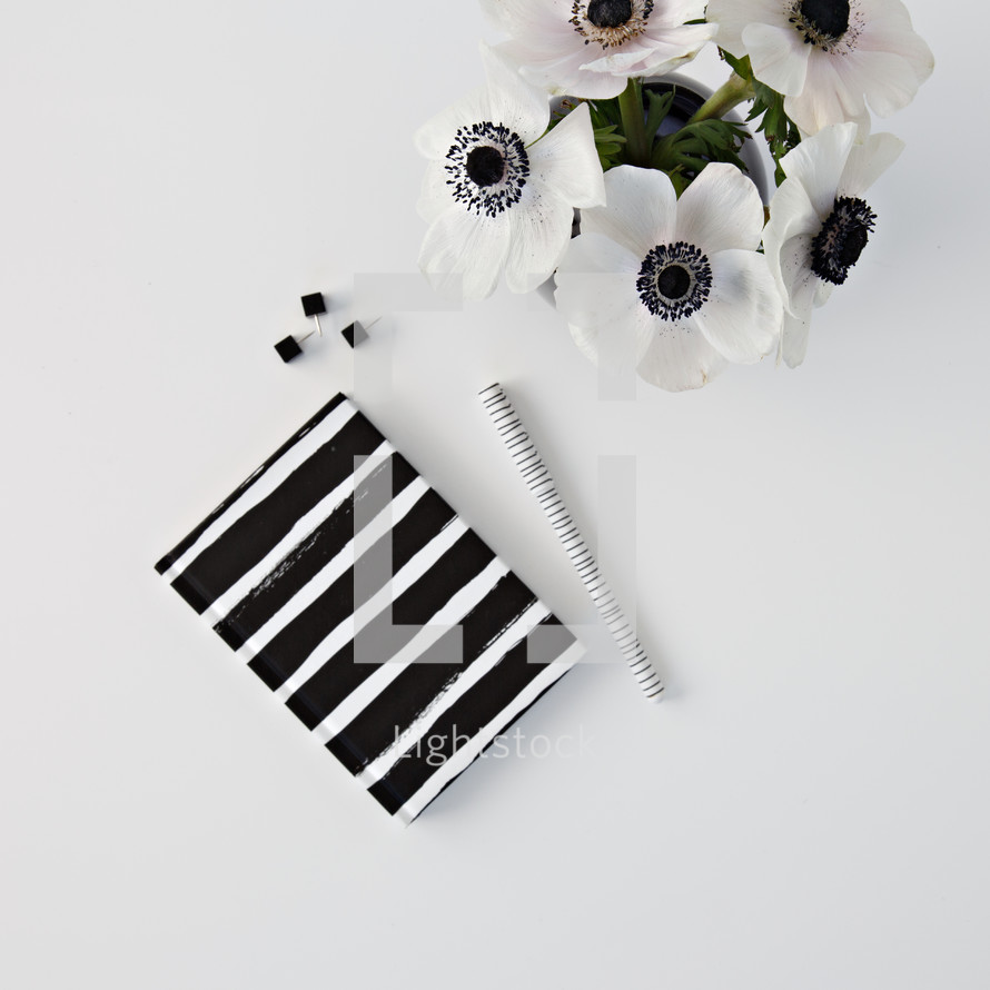 flowers in a black vase,  journal, and pens on a desk 