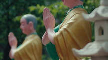 Buddha statues are holding hands and reciting Buddha's name outdoors. Static shot