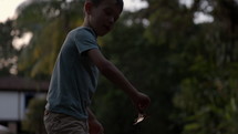 Young boy puts paper boat in stream