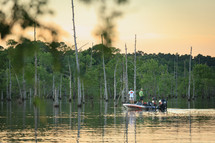 Two men fishing together in boat on lake with mangrove trees at sunset 