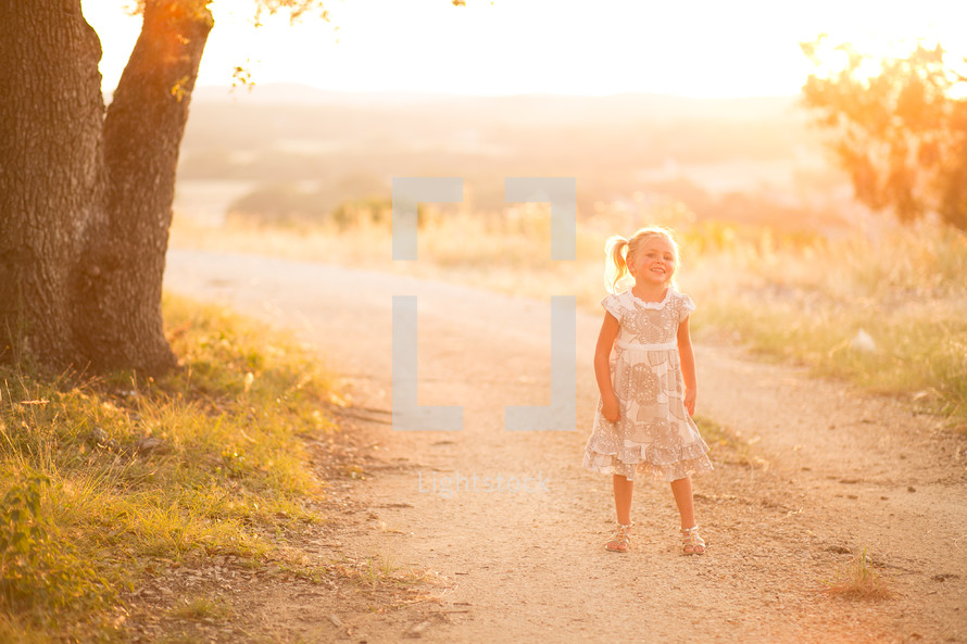 A young girl standing on a dirt road on a sunny day