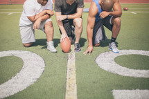 athletes kneeling in prayer on the football field 
