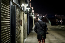 man with a camera walking on a sidewalk at night 