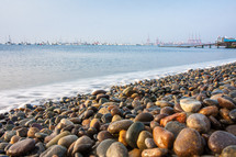colorful stones and rocks by the ocean on the shore of the beach with boats in the distance