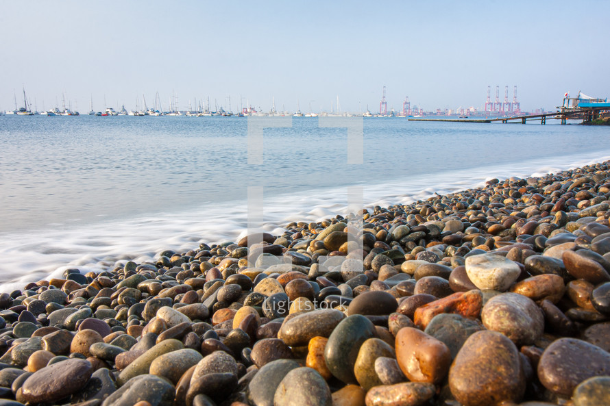 colorful stones and rocks by the ocean on the shore of the beach with boats in the distance
