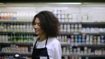 Cheerful worker in black apron dancing in supermarket, having fun during work.